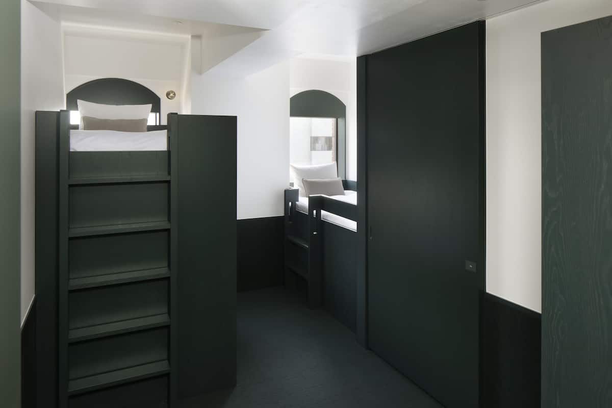 A narrow hallway with a bunk bed on the left, a desk with a chair, and a large wardrobe on the right.