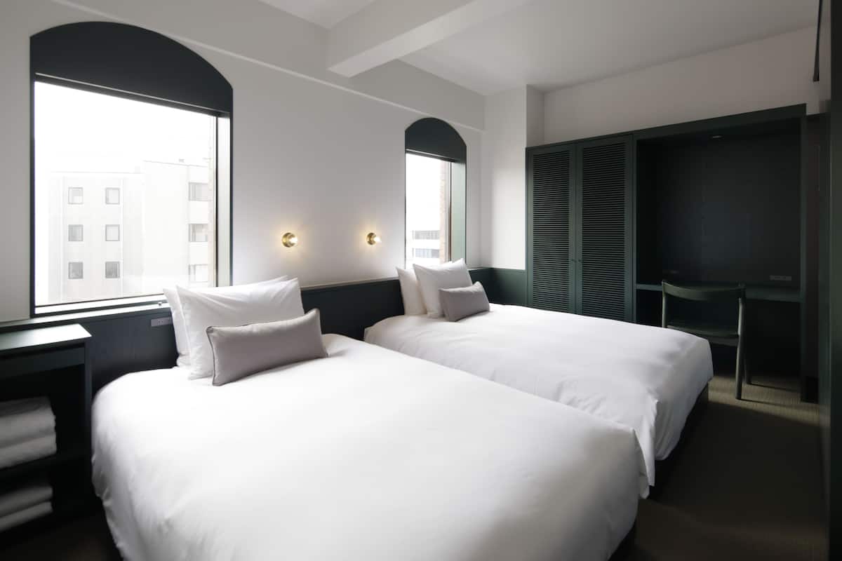 A hotel room with two beds, a desk, a chair, and a wardrobe.