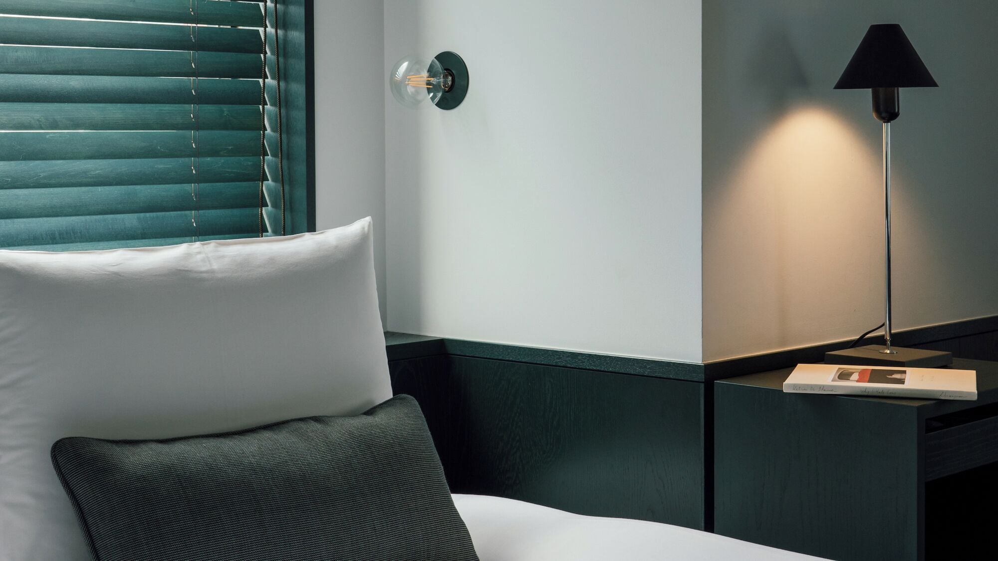 A hotel room with a bed, a nightstand, a lamp, and a wall-mounted light fixture.