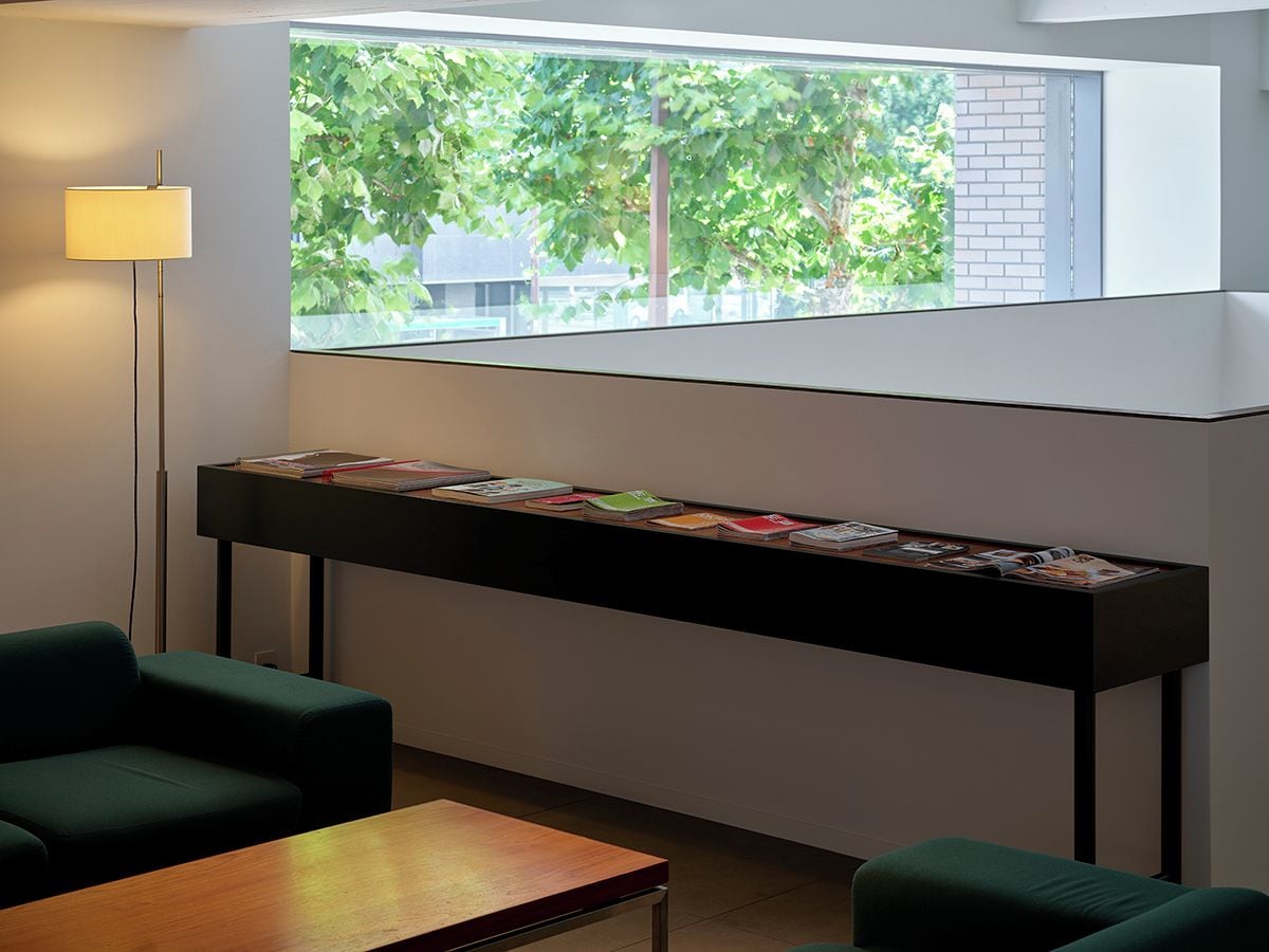 Un coin lecture avec une bibliothèque, une lampe et une vue sur les arbres par la fenêtre.