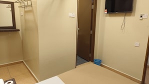 A hotel room with a bed, a television mounted on the wall, a door, and a small blue trash bin. - The Pines Hotel (Kampung Raja)