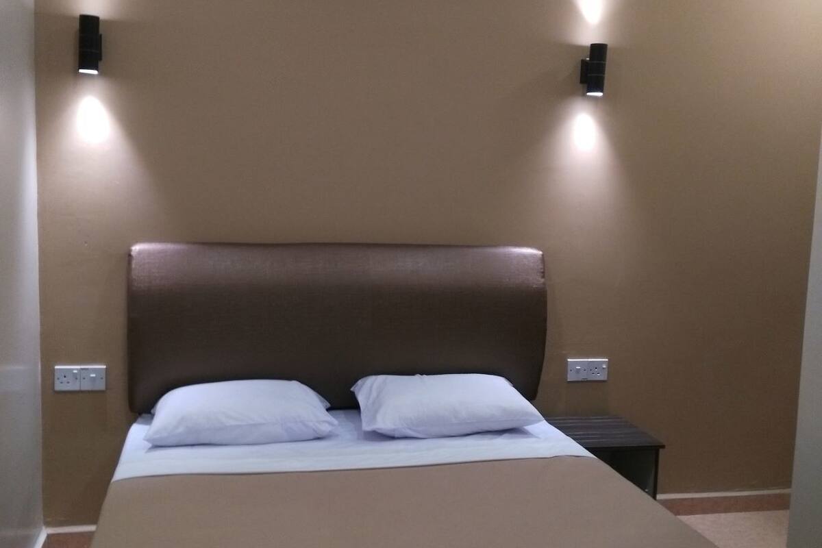 Un lit simple avec une tête de lit, deux tables de chevet et des appliques murales.