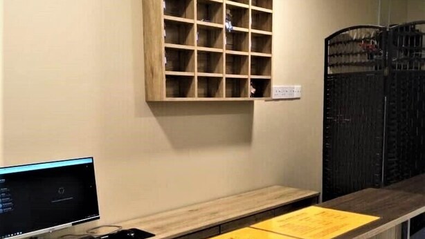 A reception desk with a computer, a wooden cabinet above it, and a black gate to the right. - The Pines Hotel (Kampung Raja)