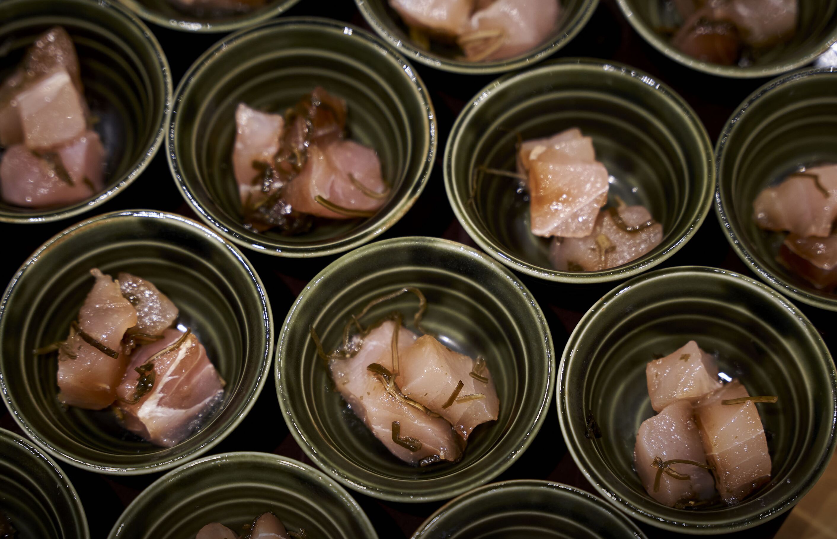 Multiple bowls containing a food item with a liquid base, possibly a soup or broth, with pieces of meat and garnish.