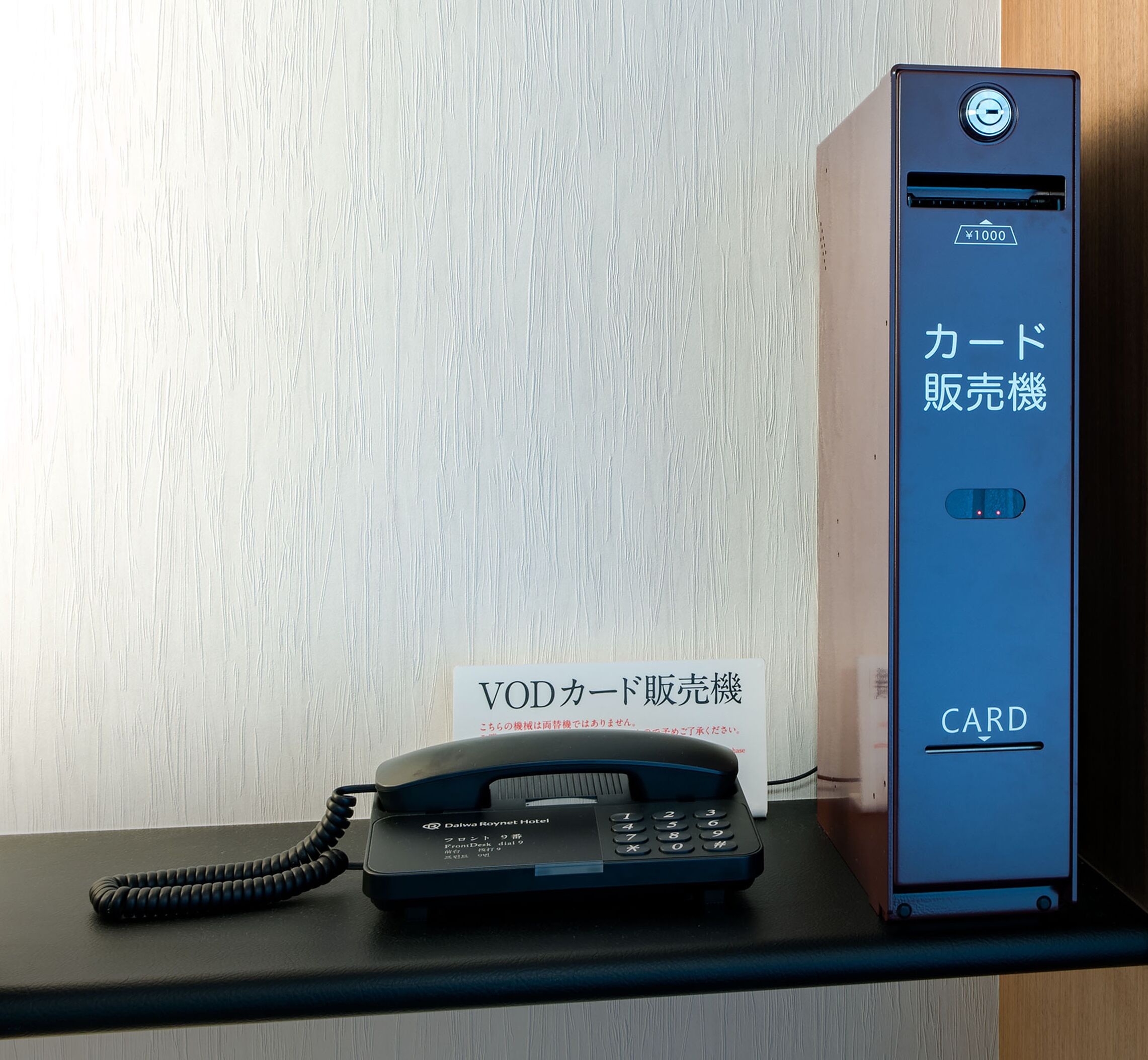 A VOD card machine and a telephone on a desk.
