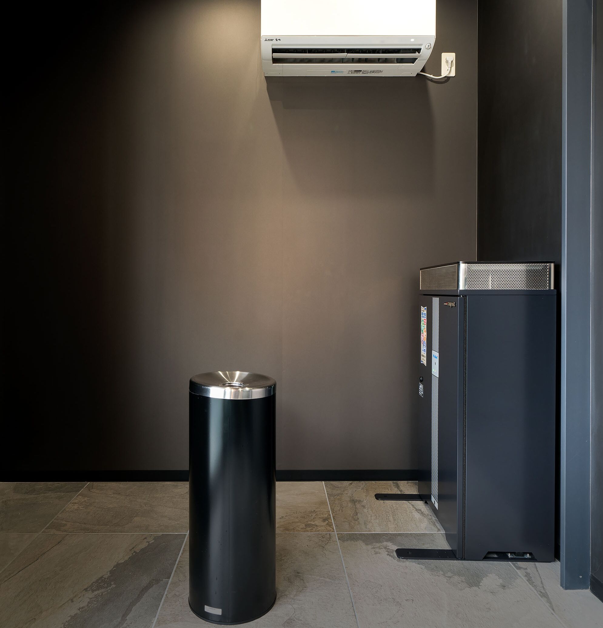 A modern bathroom with a black trash bin, a small black cabinet, and a wall-mounted air conditioner.