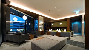 Eine moderne Hotelhalle mit grauen Sofas, einem großen Couchtisch und Pendelleuchten.