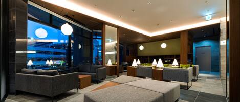 Eine moderne Hotelhalle mit grauen Sofas, einem großen Couchtisch und Pendelleuchten.