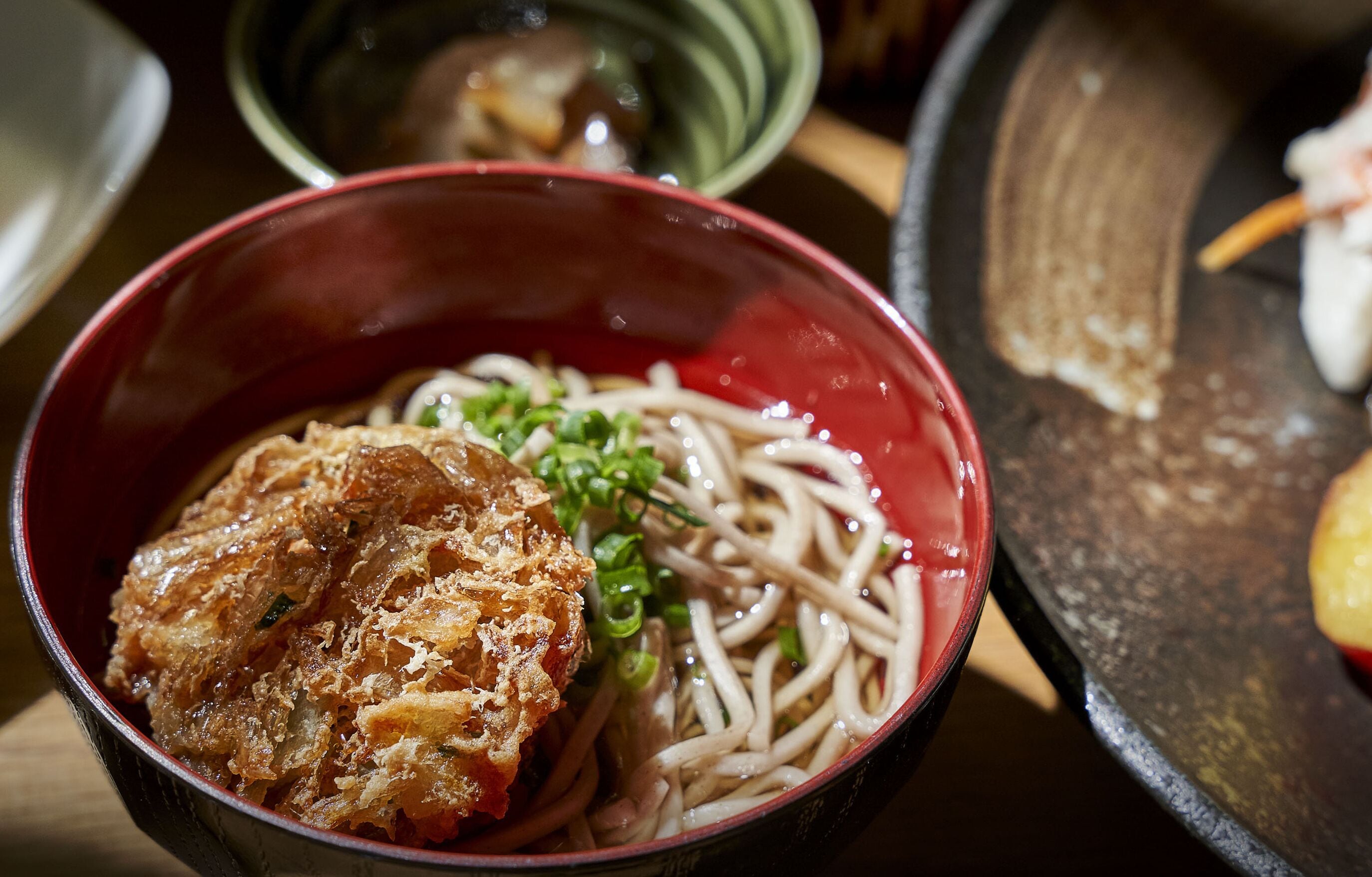 A bowl of noodles with a fried topping and green onions.