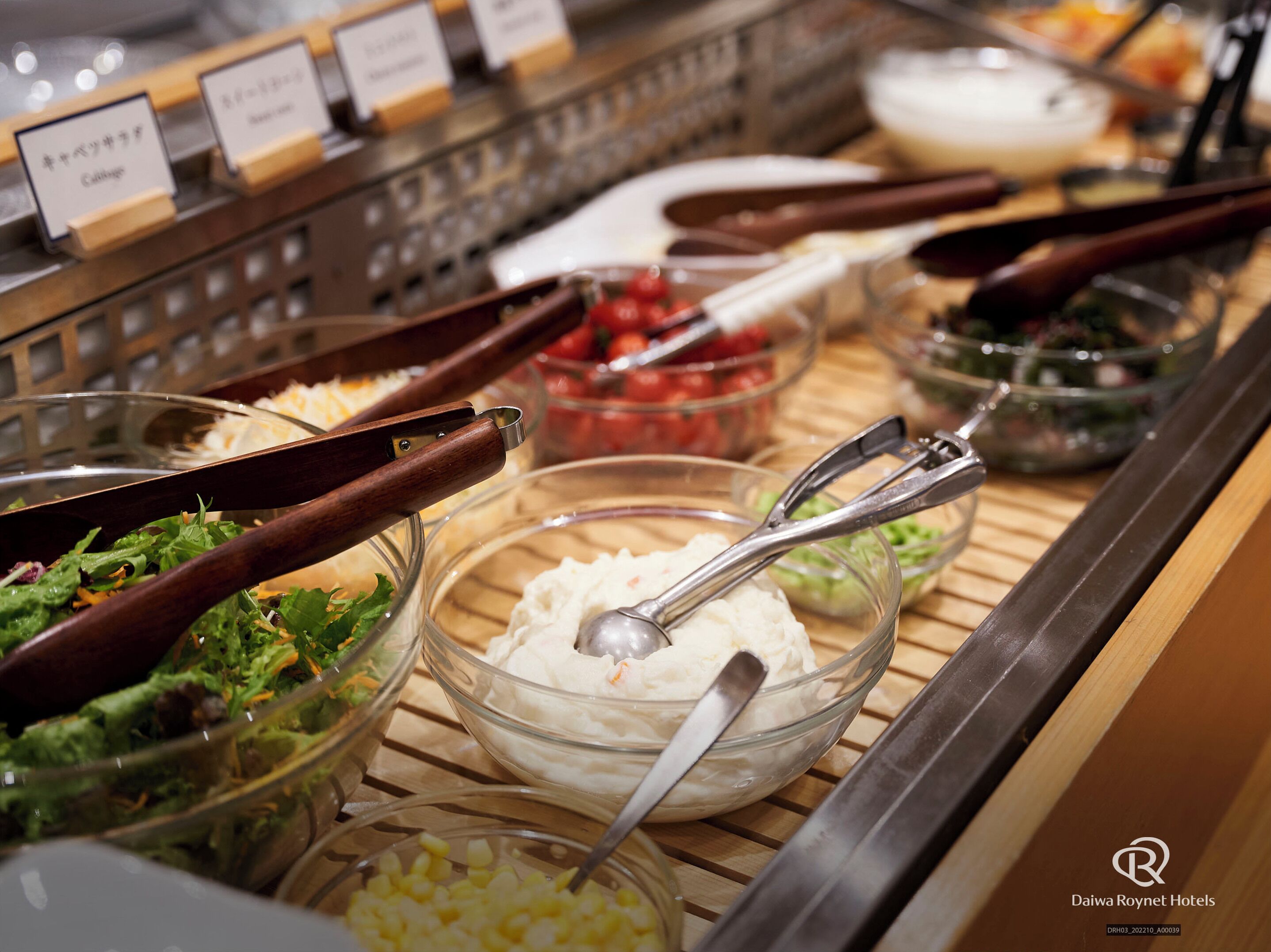 A buffet with various food options, including salads, a bowl of cream cheese, and a bowl of tomatoes.