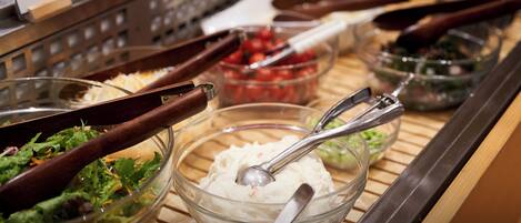 A buffet with various food options, including salads, a bowl of cream cheese, and a bowl of tomatoes.