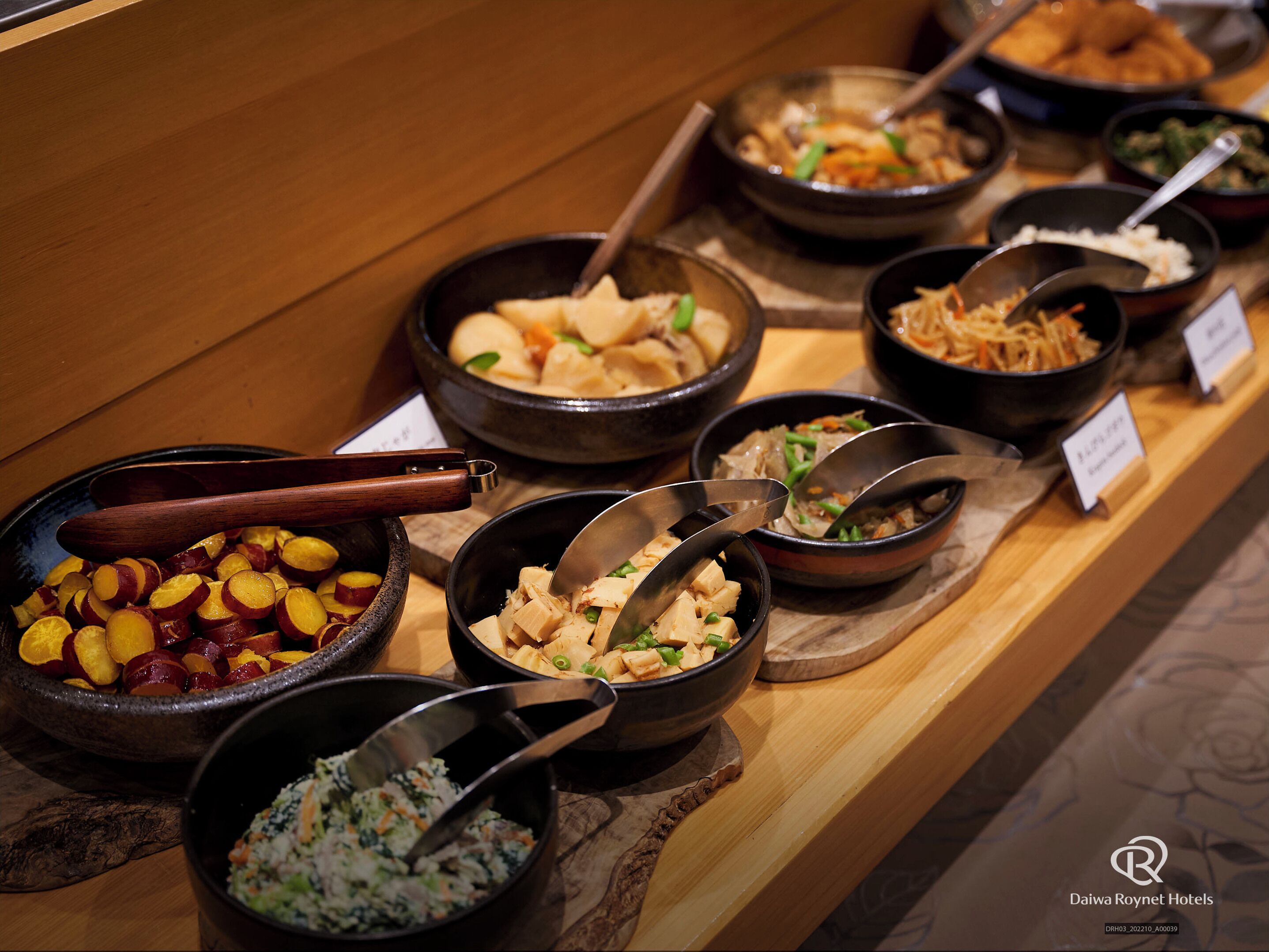 A buffet with various dishes, including fruits, vegetables, and different types of salads.