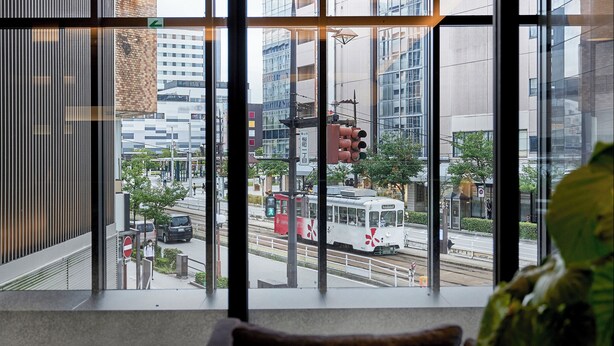 Ein modernes Hotelzimmer mit großen Fenstern und Blick auf eine belebte Stadtstraße, inklusive Straßenbahn und Gebäuden.