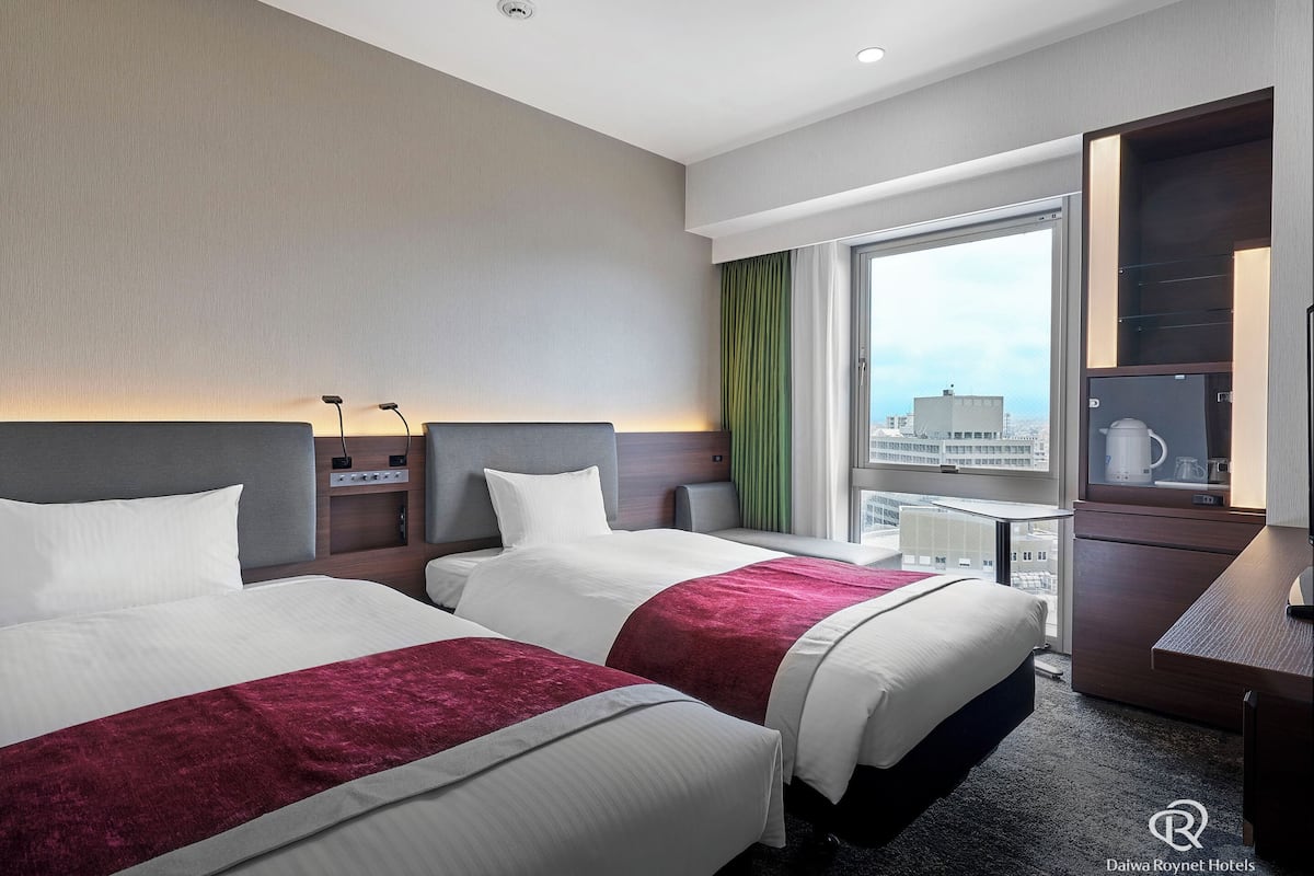 Ein Hotelzimmer mit zwei Betten, einem Schreibtisch, einer Kaffeemaschine und Blick auf die Stadt.