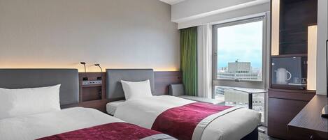 A hotel room with two beds, a desk, a coffee maker, and a view of the city.