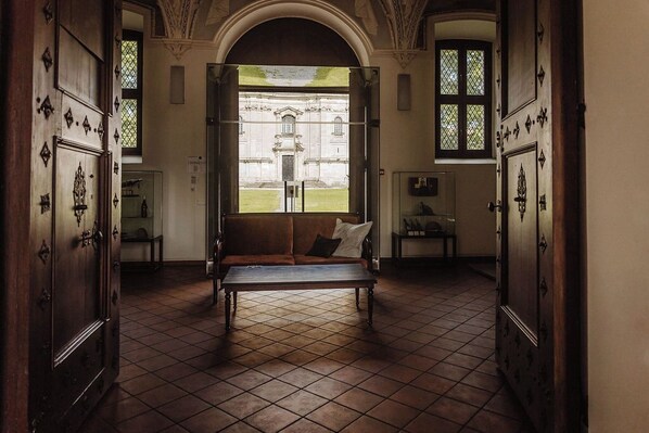 A room with a bench, a large window, and a view of a building outside. - Hotel Monte Pacis (Kaunas)