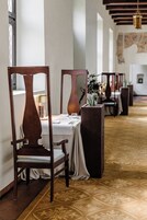 Un pasillo de hotel con sillas de madera, mesas dispuestas con manteles blancos y una alfombra estampada.