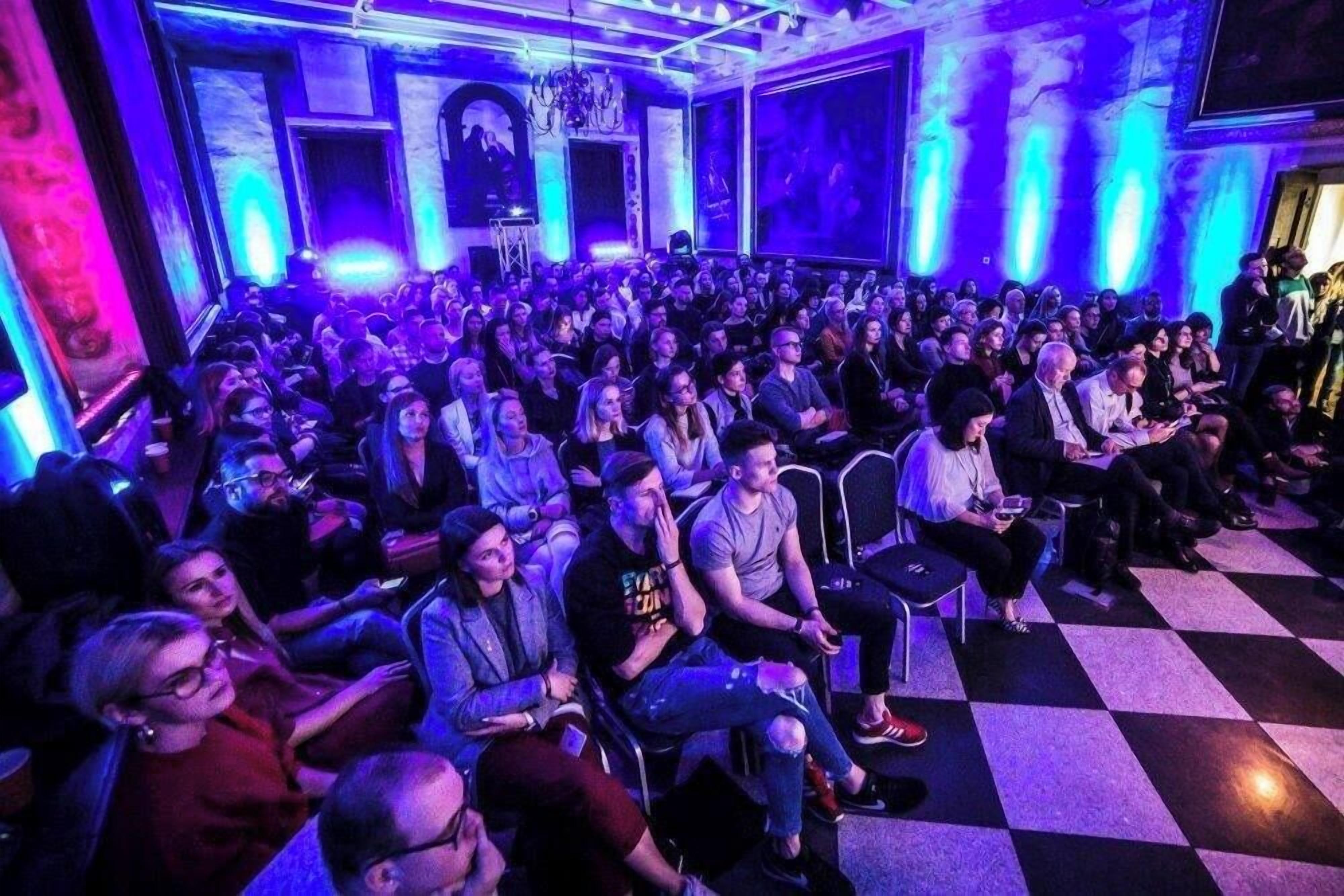 A conference room with a checkered floor, rows of chairs, and attendees seated.