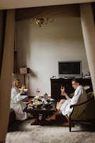Een kamer met een eettafel gedekt voor twee personen, een televisie op een standaard en een lamp.
