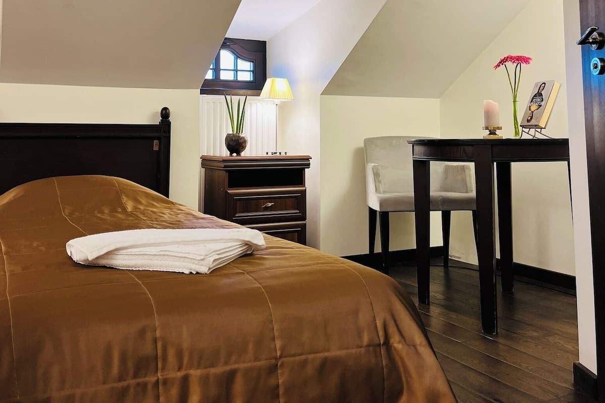 A bedroom with a bed, a desk, a chair, and a window.