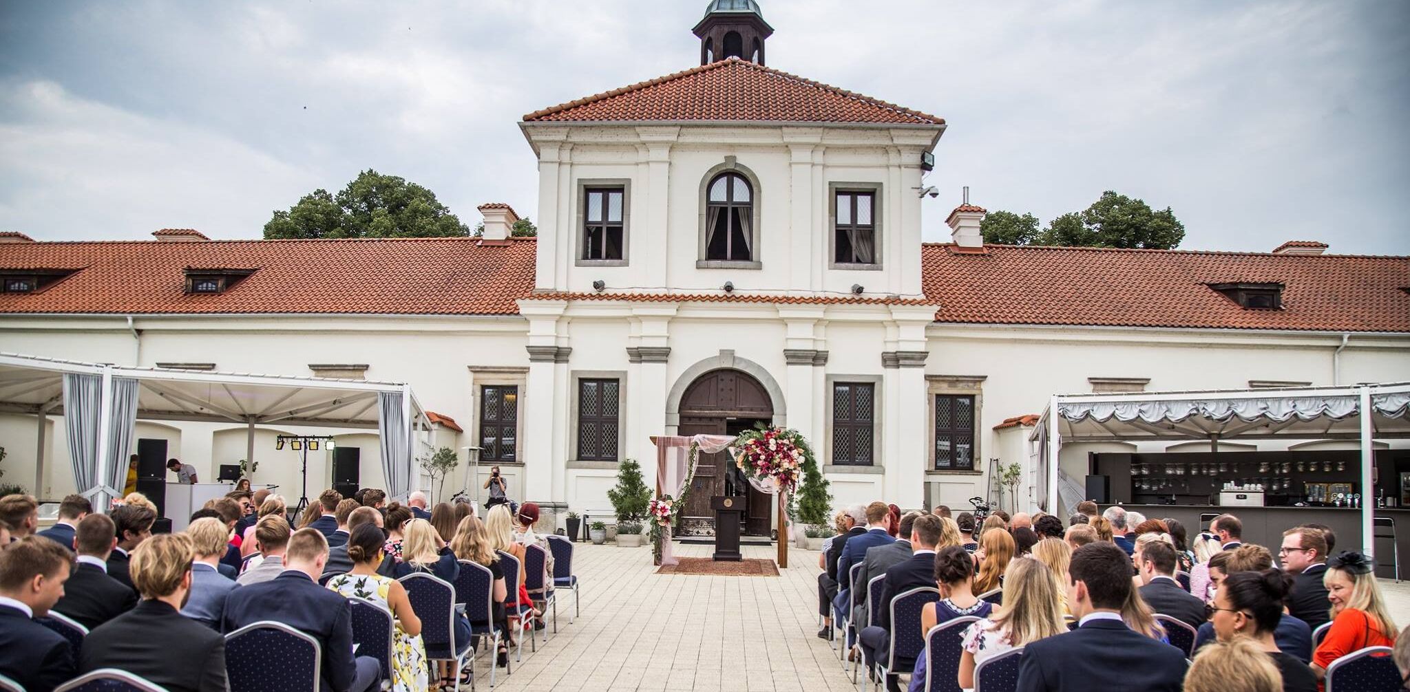 Eine formelle Veranstaltung im Freien vor einem weißen Gebäude mit roten Ziegeln und einem zentralen Bogen.