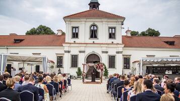 Eine formelle Veranstaltung im Freien vor einem weißen Gebäude mit roten Ziegeln und einem zentralen Bogen.