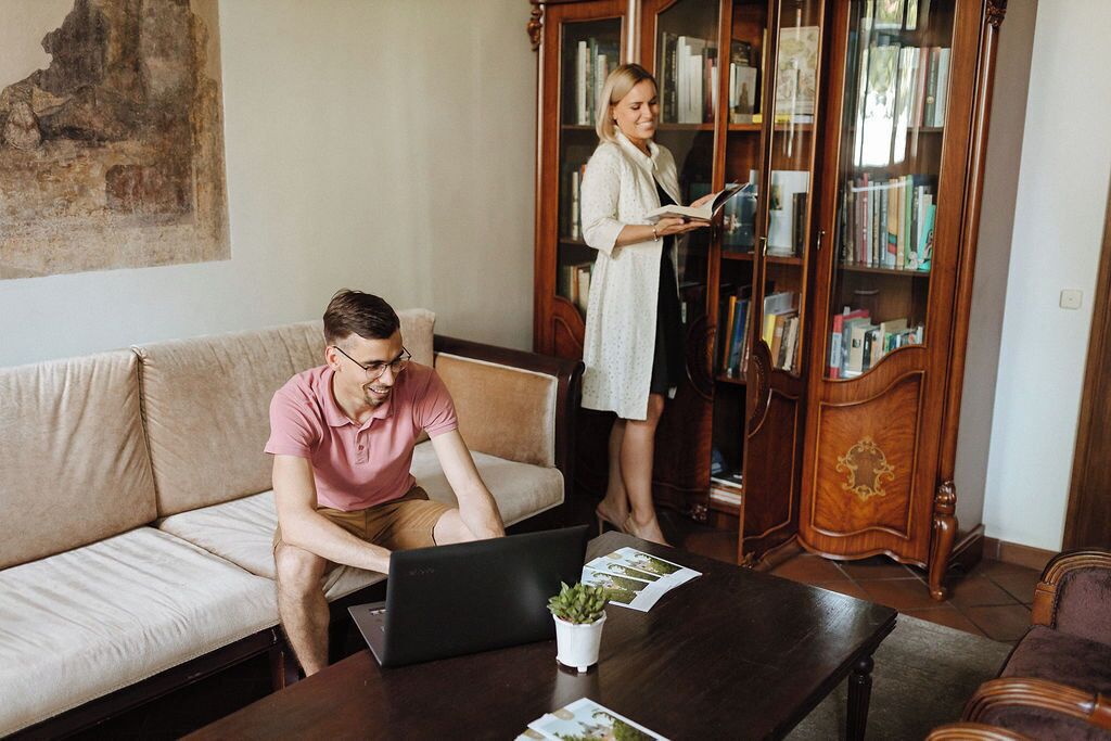 A living room with a sofa, a coffee table with a laptop and a plant, and a bookshelf filled with books.