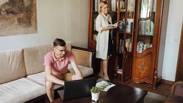 A living room with a sofa, a coffee table with a laptop and a plant, and a bookshelf filled with books.