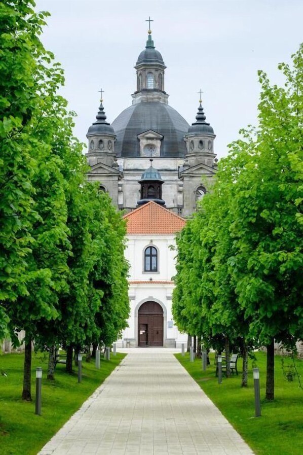 A church with a central dome and four smaller domes, flanked by trees and a paved pathway leading to the entrance.