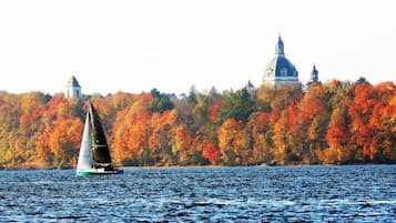 A sailboat on a lake with autumn foliage and a building in the background.