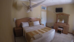 A hotel room with a bed, a wooden nightstand, a dresser, a mirror, and a ceiling fan. - Golden Days Executive lodge (Lusaka)
