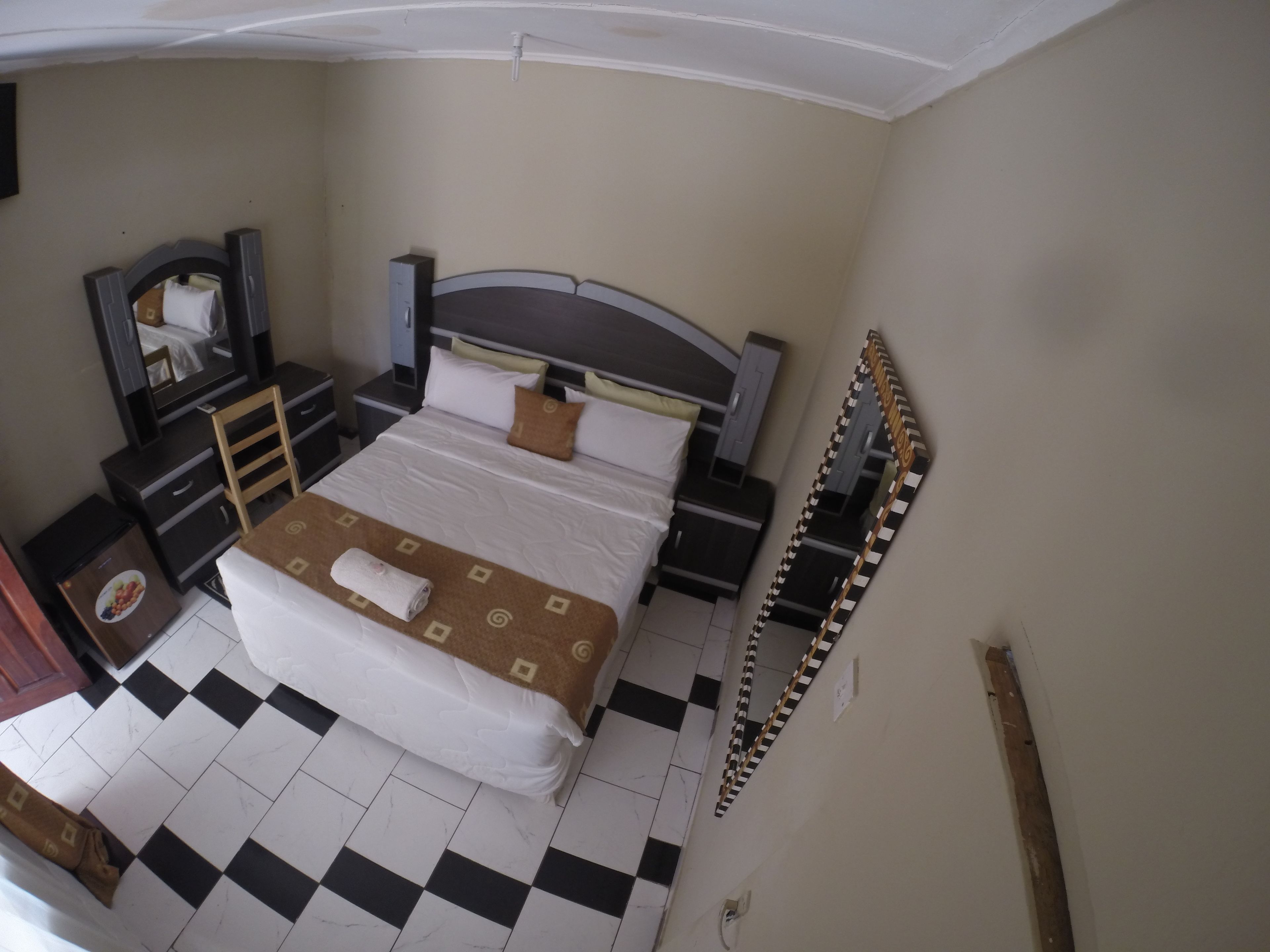 A hotel room with a bed, a desk, a chair, a dresser, a mirror, and a small trash bin.