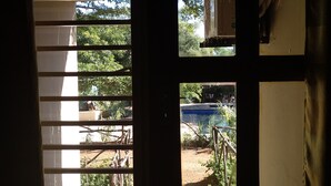 A window with blinds, a view of greenery outside, and a glimpse of a pool area. - Golden Days Executive lodge (Lusaka)