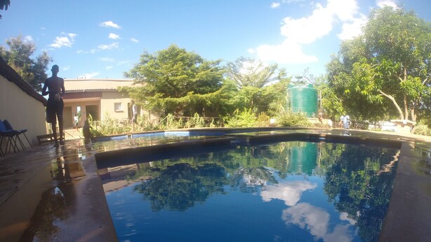 A swimming pool with clear blue water, surrounded by trees and a building. - Golden Days Executive lodge (Lusaka)
