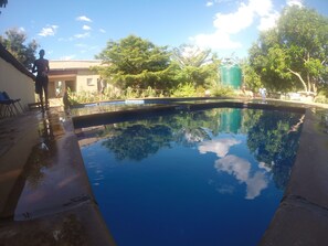 A swimming pool with clear blue water, surrounded by trees and a building. - Golden Days Executive lodge (Lusaka)