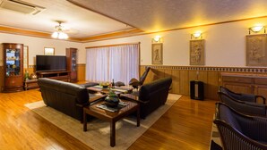 A living room with a sofa, coffee table, and TV. There are wall sconces and framed artwork. - VILLA Kano (Okinawa)