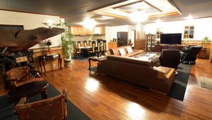 A spacious living room with a large sofa, a dining area with chairs, a kitchen in the background, and a television. - VILLA Kano (Okinawa)