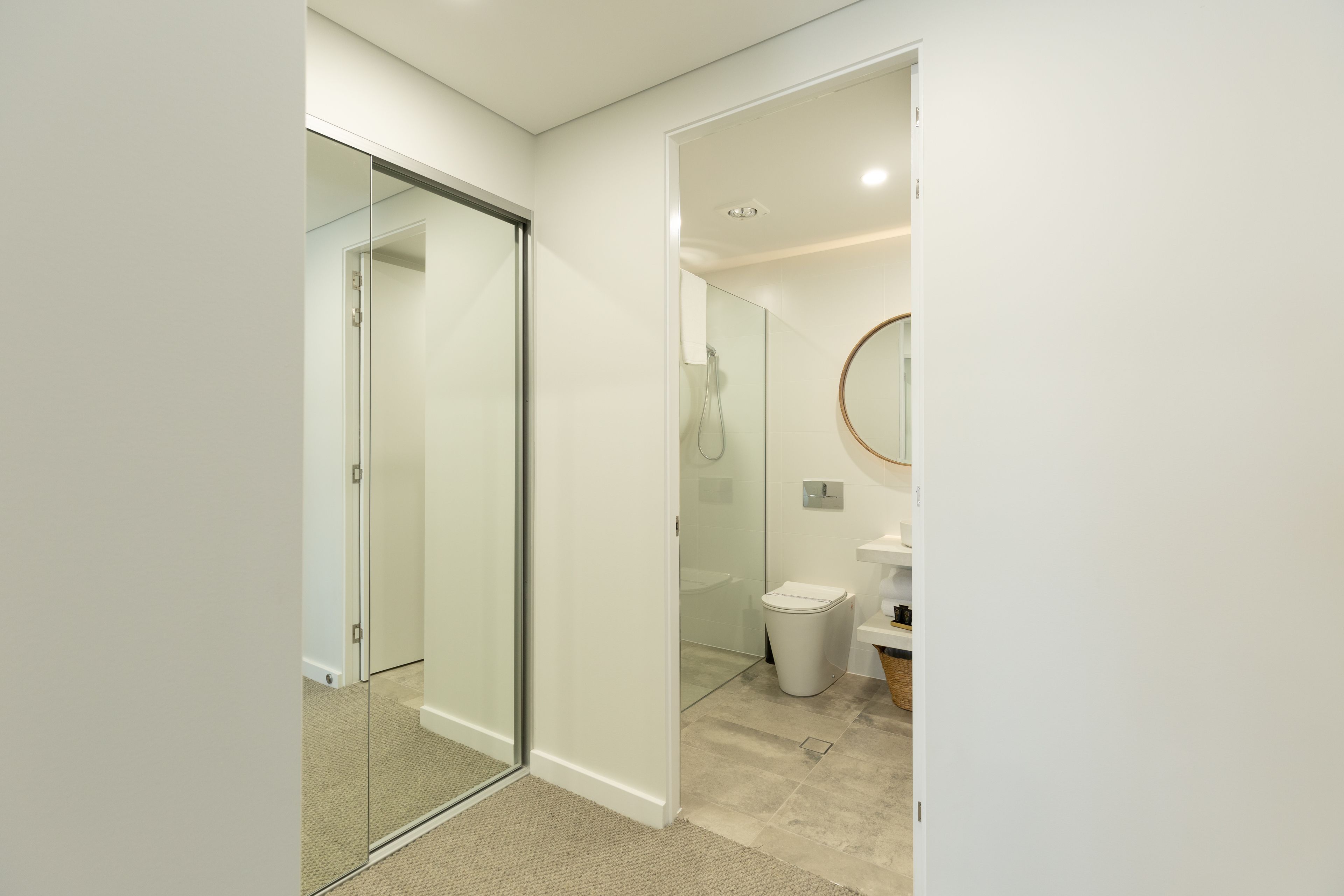 A modern bathroom with a glass shower enclosure, a toilet, and a sink with a round mirror.