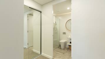 A modern bathroom with a glass shower enclosure, a toilet, and a sink with a round mirror.