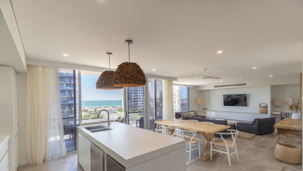 Une cuisine moderne dotée d’un grand îlot central, d’un coin repas avec une table en bois et d’une vue sur l’océan.