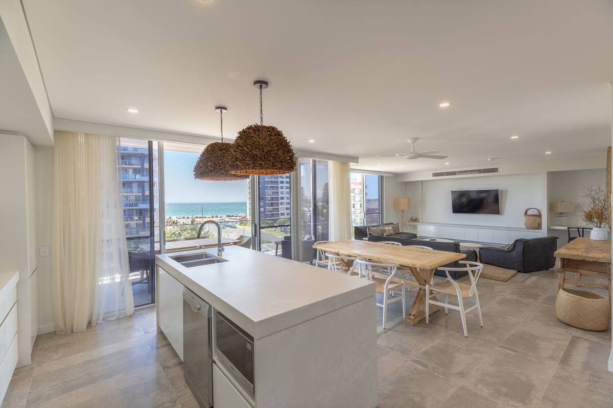 A modern kitchen with a large island, a dining area with a wooden table, and a view of the ocean.