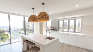Une cuisine moderne dotée d’un grand îlot central, de deux luminaires suspendus et offrant une vue sur la ville grâce à de grandes fenêtres.