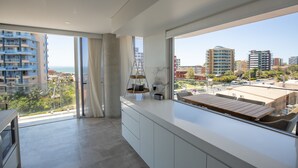 Une chambre d’hôtel moderne avec balcon, de grandes fenêtres et une vue sur le paysage urbain.