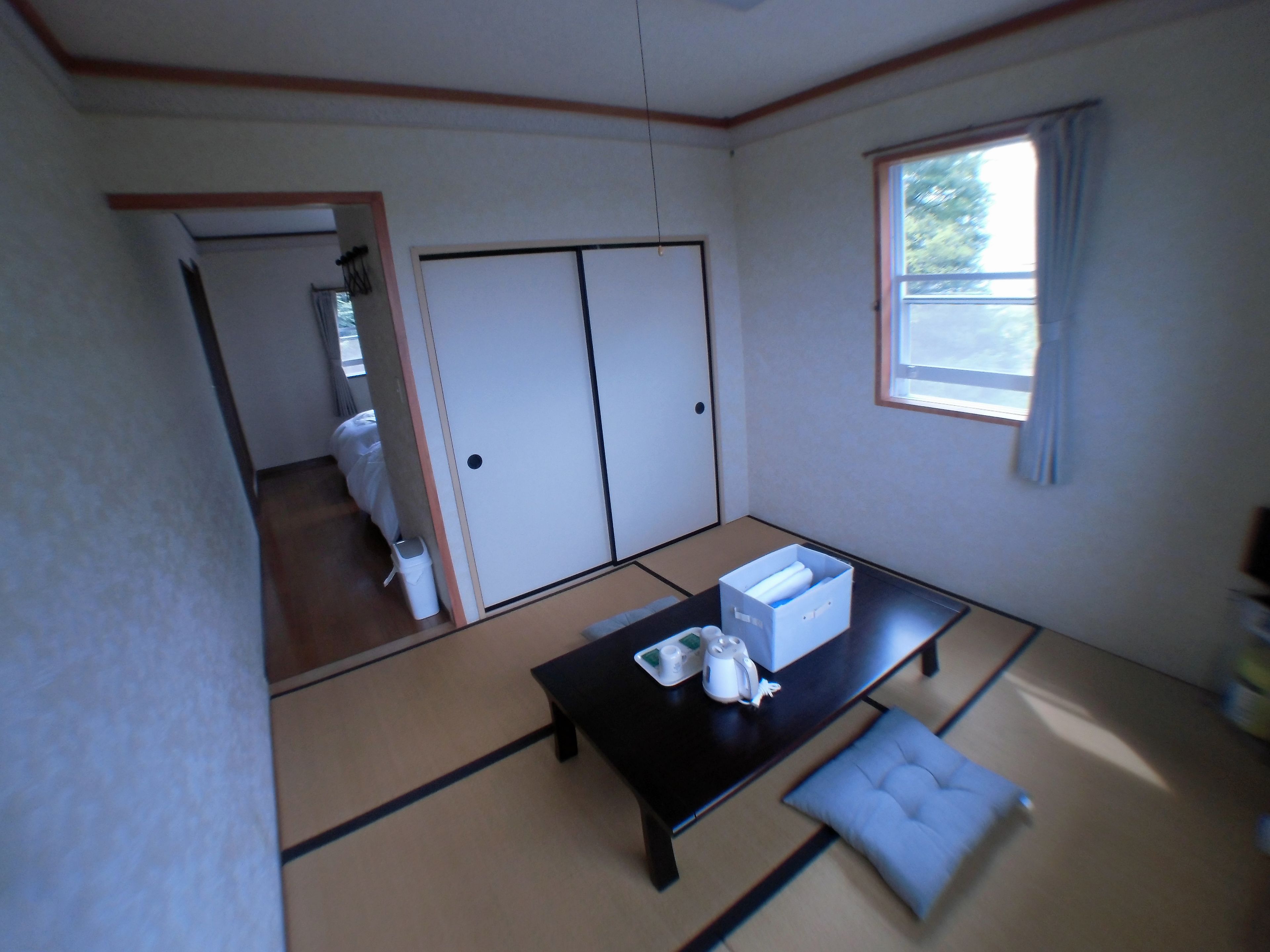 A traditional Japanese room with tatami flooring, a low table with a cushion, a sliding door, and a window with curtains.