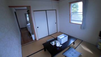 A traditional Japanese room with tatami flooring, a low table with a cushion, a sliding door, and a window with curtains.