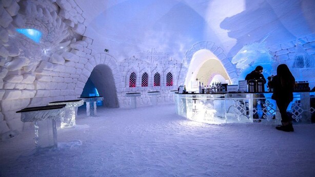 An ice bar with tables and a counter, surrounded by ice walls and arches. - Camp Adventure (Jukkasjarvi)