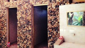 A room with walls covered in pebbles, wooden doors, and a tiled bench area. - Mai Chau Xanh Bungalow (Mai Ha)
