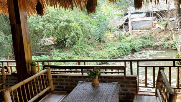 A bamboo-framed outdoor seating area with a table and chairs, overlooking a garden and a small stream. - Mai Chau Xanh Bungalow (Mai Ha)