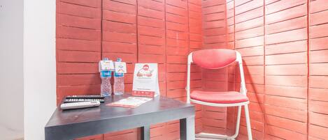 A corner with a red wall, a white chair, a table with a remote control, and a poster.