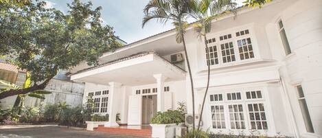 A white colonial-style building with a covered porch, a tiled roof, and a paved driveway.